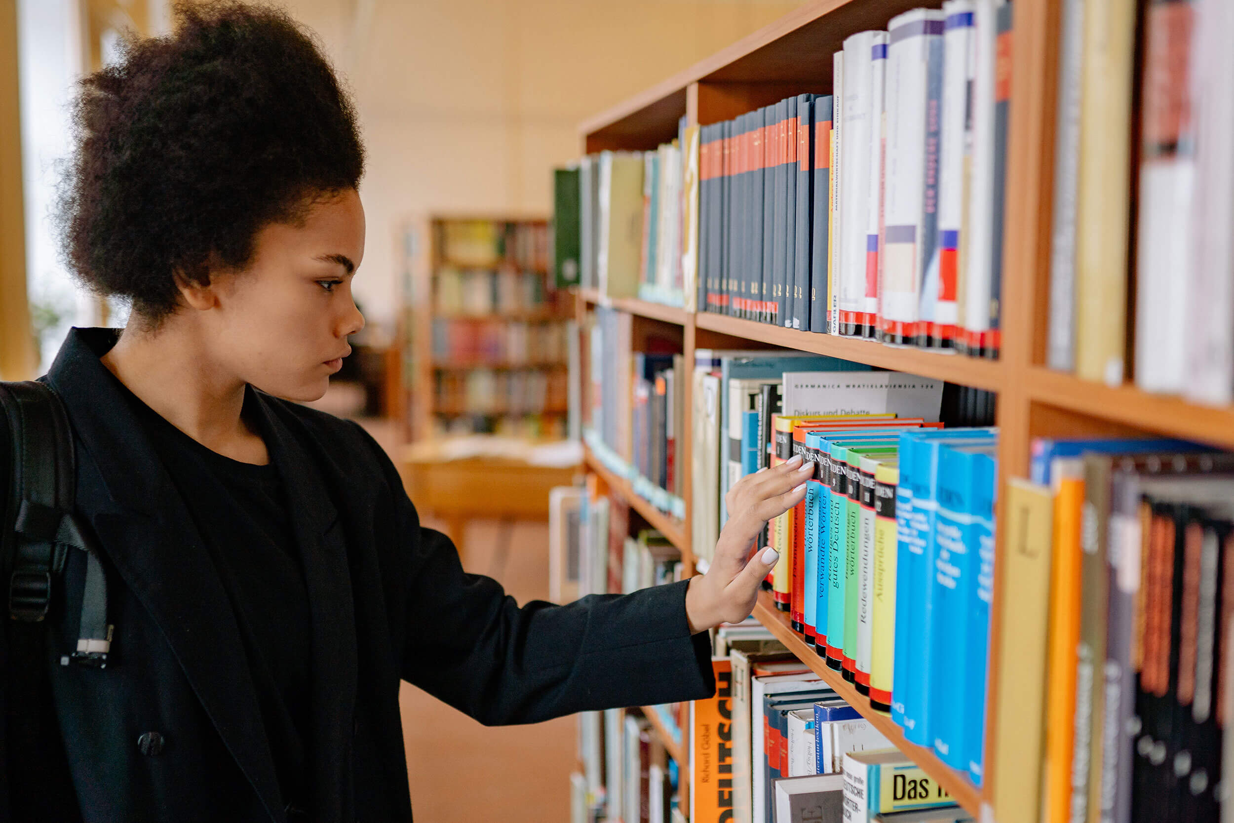 female student surveys bookshelf in college library